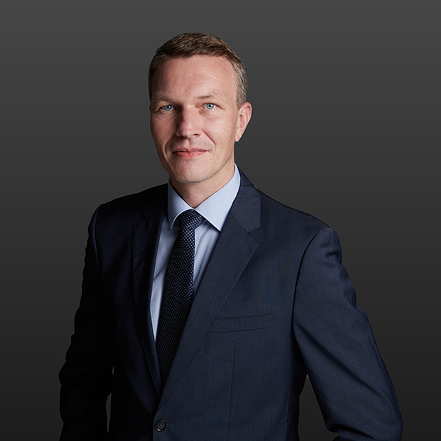 Das Bild zeigt Henning Vogelsang. Er trägt einen dunklem Anzug mit Kravatte und Hemd.