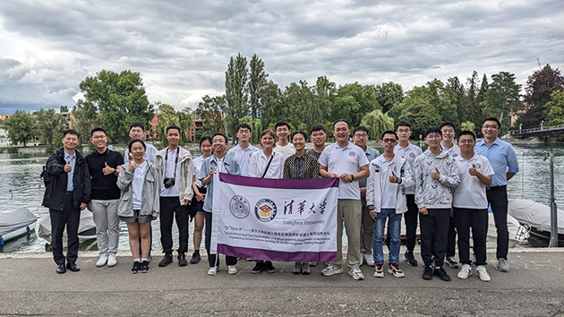 Eine große Gruppe von jungen Menschen aus China, die vor einem Fluss stehen. Sie halten eine Fahne ihrer Universität hoch.