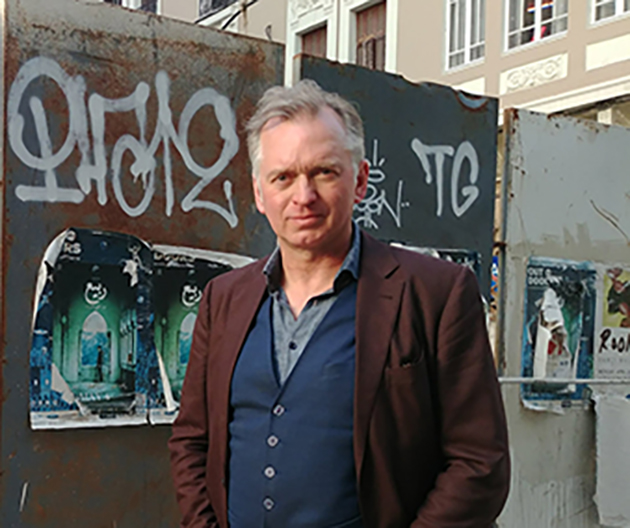 Christian Springer steht in brauner Jacke vor einer Graffiti-Wand