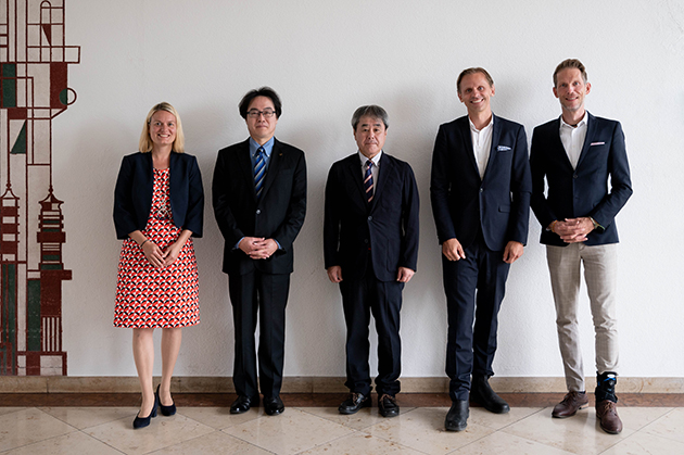 Das Bild zeigt die Delegation mit Vertreterinnen und Vertretern der Hochschule Konstanz. Sie stehen elegant gekleidet in dunklen Anzügen vor einer Wand für das Gruppenfoto.