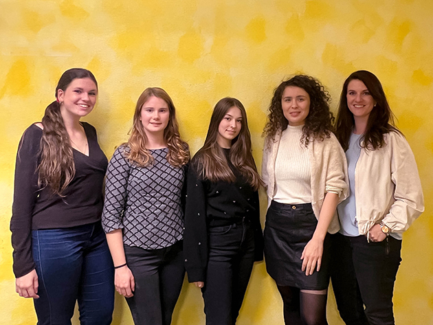 Fünf junge Frauen stehen als Gruppe vor einer gelben Wand