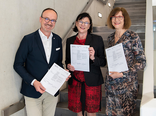 Das Bild zeigt Oberbürgermeister Uli Burchhardt, Prof. Sabine Rein und Prof. Katharina Holzinger. Sie halten jeweils ein Exemplar des Vertrags in der Hand und lächeln in die Kamera.