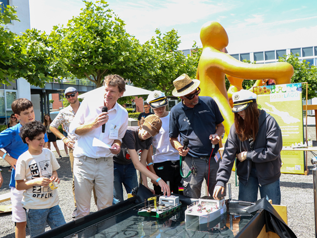 Das Bild zeigt zwei Teams und ihre Solarboote kurz vor dem Start. Die Boote liegen im Wasser und warten darauf loszufahren
