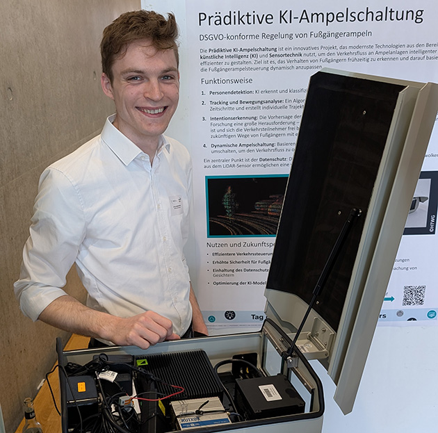 Ein junger Mann lacht in die Kamera und hat ein technisches Gerät vor sich