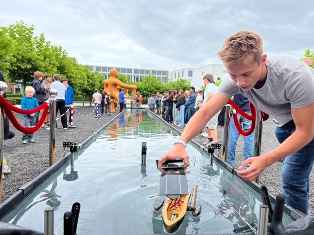 Ein Solarboot, gebaut aus einer Nussschale, wird von einem blonden Jungen in die Wasserrennbahn gesetzt