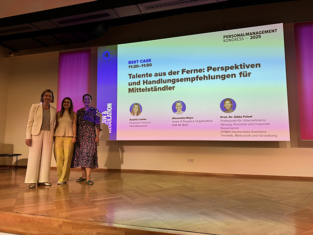 Drei Frauen stehen auf einer Bühne mit einer großen Präsentation im Hintergrund