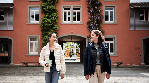 Zwei jugendliche Frauen laufen vor einem roten Gebäude auf die Kamera zu