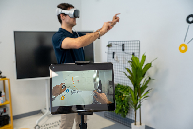 Ein Mann trägt eine VR-Brille und steht in einem Büro mit zwei Bildschirmen