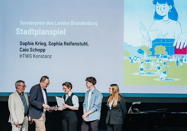 2 Männer verleihen drei Studierenden auf einer Bühne eine Urkunde