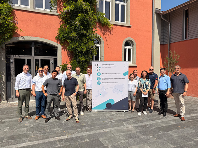 Gruppenfoto von 15 Personen vor der Bibliothek der HTWG Konstanz, in der Mitte ein Roll-up mit den Asienstudiengängen der Hochschule