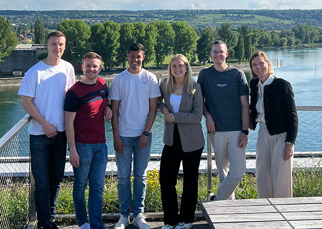 Sechs Personen stehen nebeneinander Terrasse, im Hintergrund der Rhein, Bäume und Häuser.