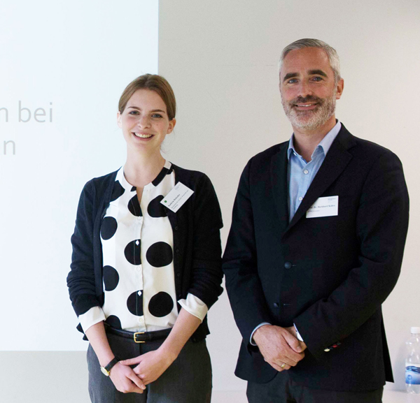 Kathrin Holzeder und Prof. Dr. Burkhard Kahre stehen vor einer Wand, an die eine Präsentationsfolie projeziert wird. Zu sehen ist nur der Rand der Folie.