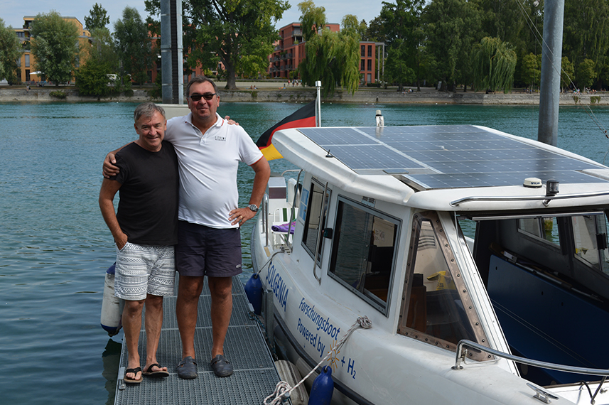 Die Crew der Solgenia, Dr. Alexander Kirjuchin und Thomas Strobel, stehen auf einem Steg. Daneben schwimmt die Solgenia im Wasser.. 