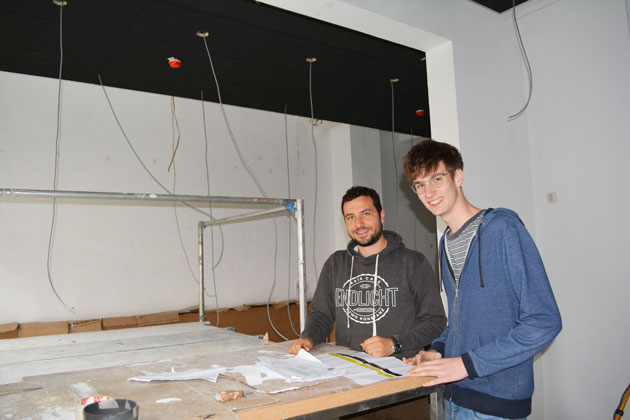 Zwei junge Männer stehen hinter einem Tisch auf einer Baustelle.