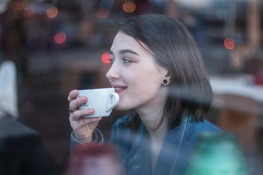 Eine junge Frau hält eine Tasse in der Hand. Sie führt sie zum Mund.