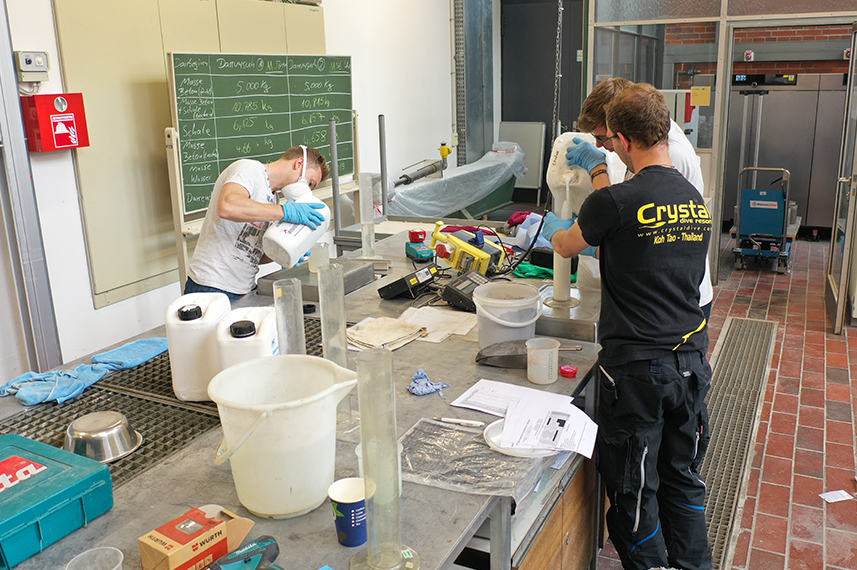 Drei Studenten stehen an einem Labortisch und arbeiten zusammen. Im Hintergrund ist eine grüne Tafel.