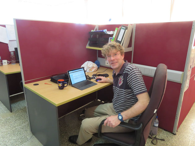 Prof. Dr. Benno Rothstein sitzt an einem Schreibtsich vor rotbraunen Wänden und dreht sich zum Fotografen hin. 