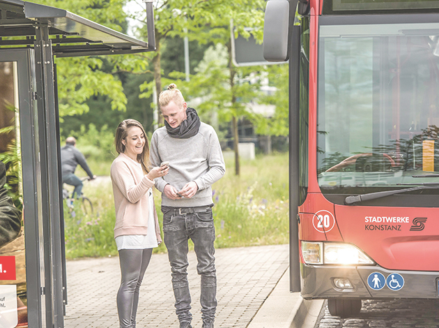 Junge Personen stehen neben einem roten Bus der Stadtwerke Konstanz