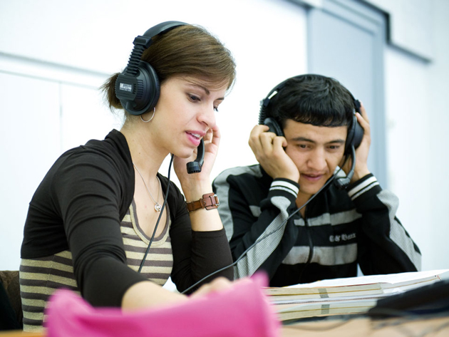 Zwei Studierende sitzen mit Kopfhörer auf dem Kopf vor einem Laptop.