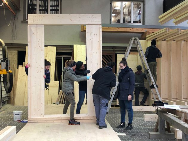 Eine Gruppe von vier jungen Menschen arbeitet in einer Zimmerei an einer Holz-Türzarge.