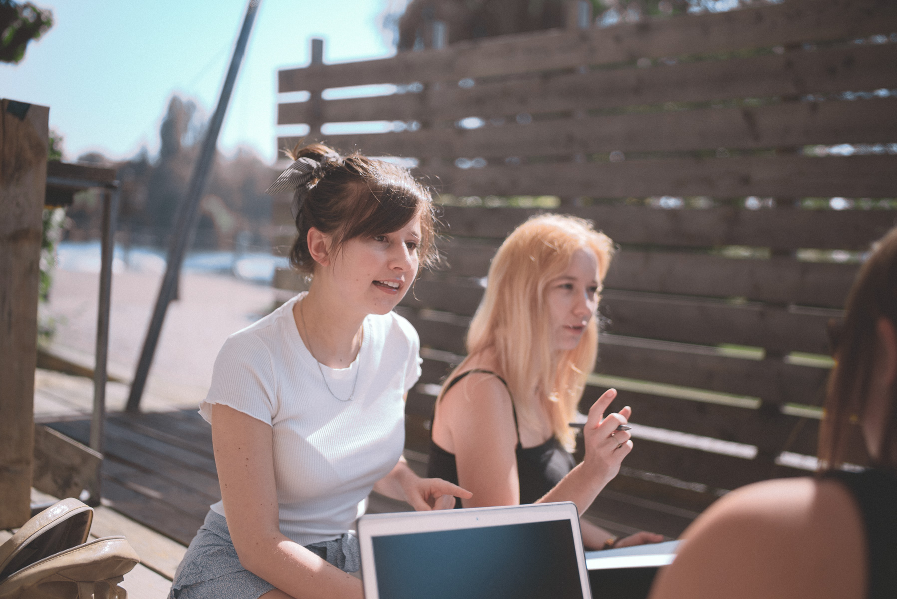 Eine Gruppe junger Frauen sitzt mit augeklapptem Laptop in der Strandbar. Die Frauen unterhlaten sich.
