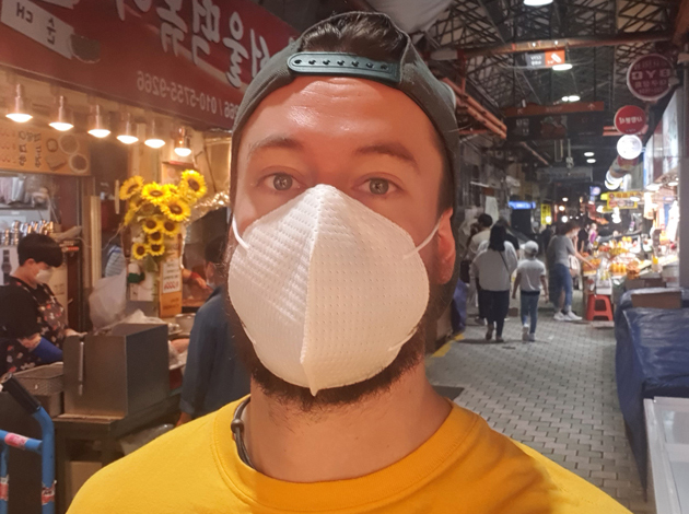 Portrait von Andreas Kustermann in einer Einkaufsstraße in Südkorea. Er trägt eine weiße Mund-Nasen-Maske.