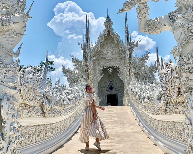 Nina Ruoff geht über einen Weg zu einem weißen Tempel im Zuckerbäckerstil und blick dabei zur Kamera zurück.