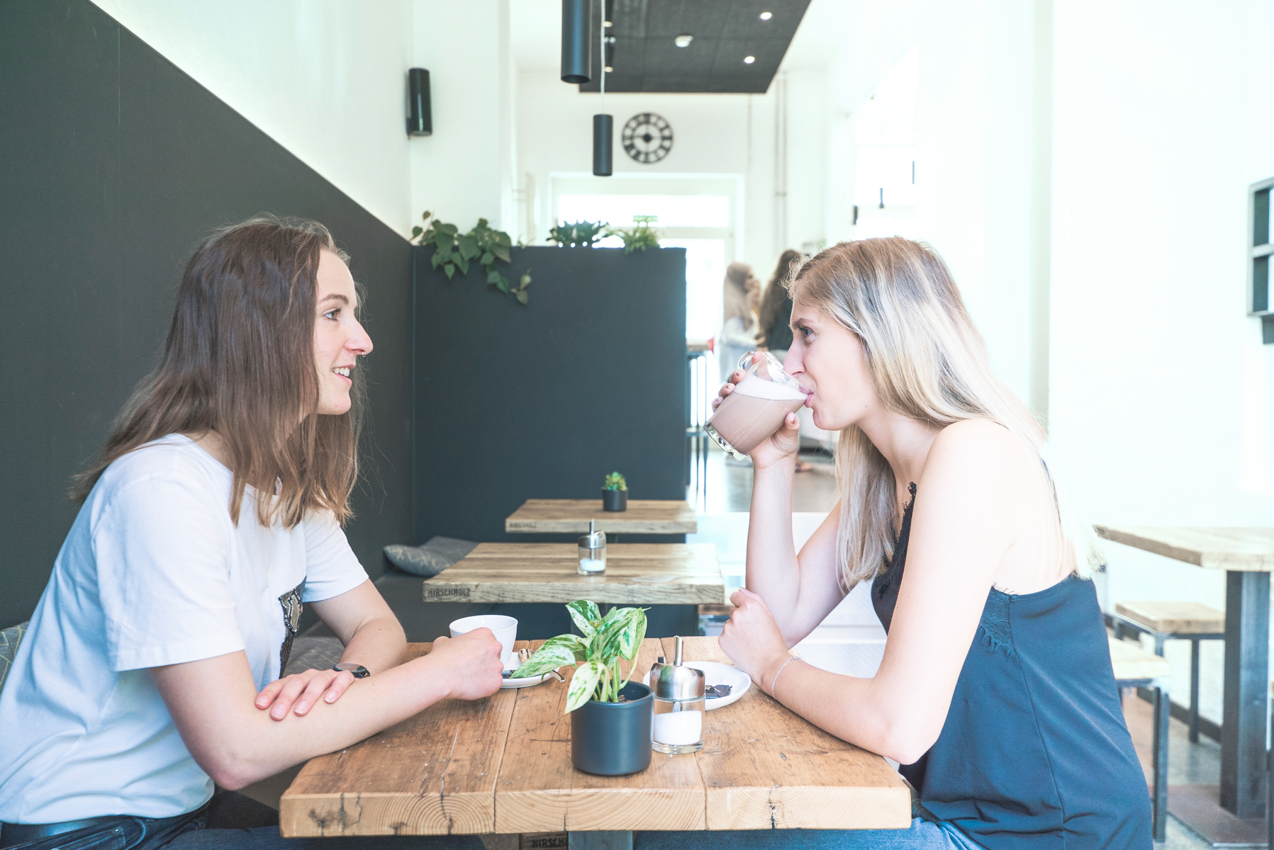 Zwei junge Frauen sitzen an einem Holztisch im Café Endlicht auf dem HTWG Campus und trinken Kaffee.