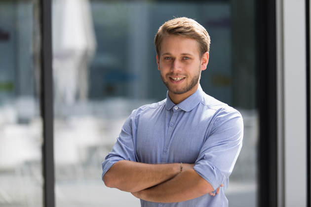 Querformatiges Portrait von Chrioph Selig. Er steht mit verschränkten Armen vor unscharfem Hintergrund und blickt in die Kamera.