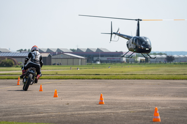 Ein Motorrad fährt zwischen Pilonen Slalom. Im Hintergrund fliegt ein Helikopter.