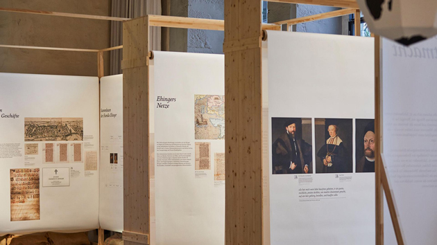Blick in einen Ausstellungsraum mit Tafeln, auf denen historische Texte und Bilder zu sehen sind.