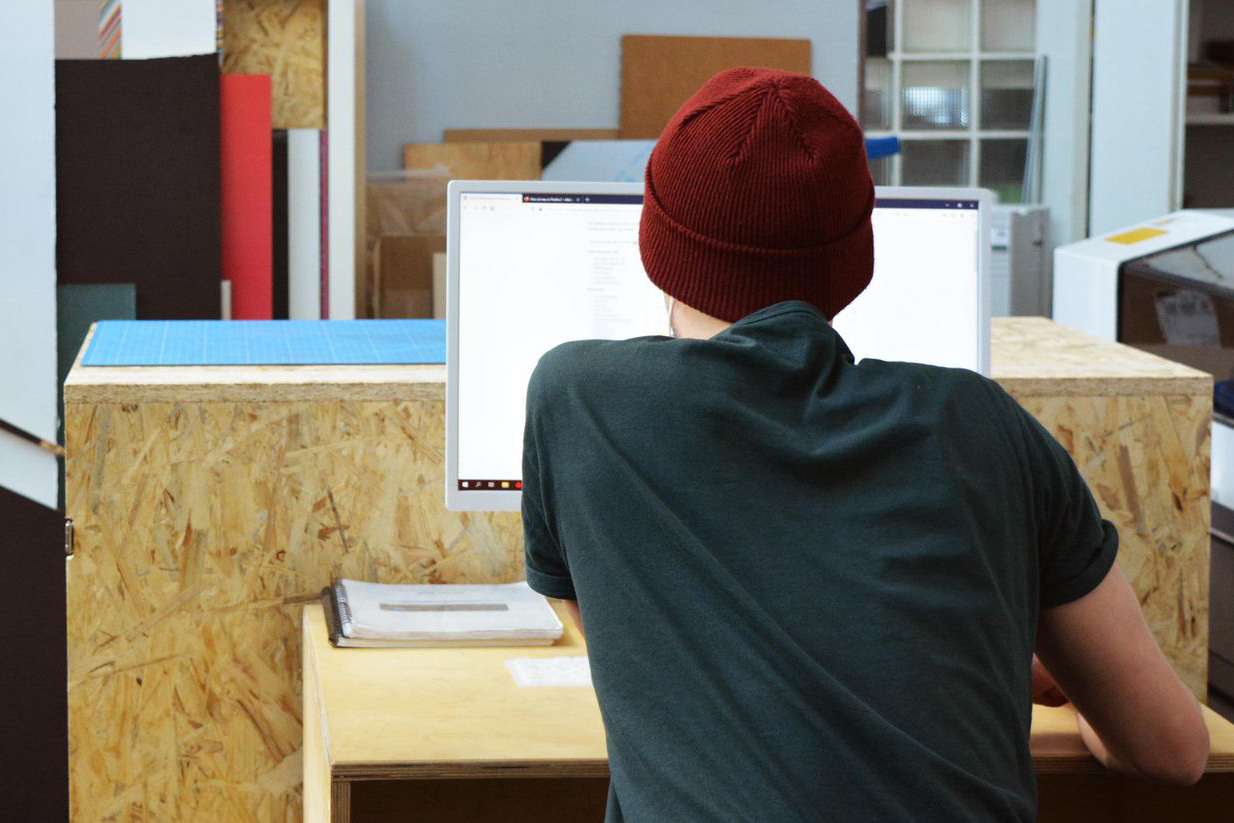 Ein junger Mann sitzt mit dem Rücken zum Betrachter an einem PC.