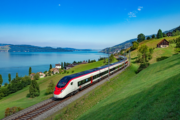Blick aus der Vogelperspektive auf einen roten Zug, der durch eine Schweizer Alpenlandschaft fährt.