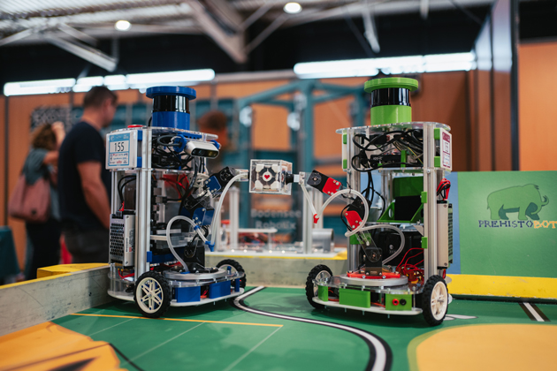 Zwei Roboter halten mit ihren Greifarmen ein Plastikkästchen und sind darüber verbunden. Auf dem Plastikkästchen leuchtet ein rotes Herz.zwischen sich