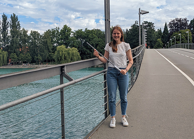 Eine Bauingenieurwesen-Studentin steht auf einer Brücke und hält einen Meterstab in der Hand.