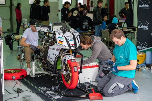 Eine Gruppe junger Menschen steht neben einem Rennmotorrad und bastelt an der Maschine. Inmitten der Gruppe steht in Motorradkleidung Studentin Hannah Schienle.