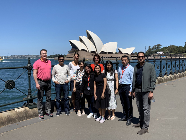 Eine Gruppe von rund 15 Personen blickt in die Kamera. Dahinter ist die Oper von Sydney zu sehen. 