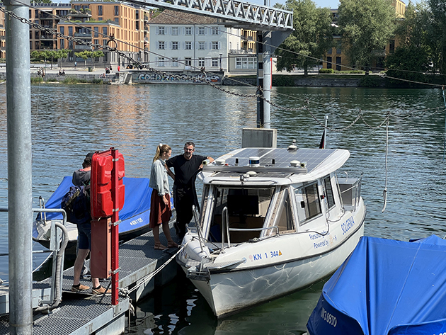 Das Foto zeigt ein Forschungsboot an einem Bootsanleger. Zwei Personen stehen daneben und unterhalten sich.