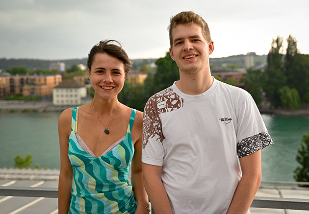 Eine junge Frau und ein junger Mann stehen auf einem Dach und lächeln in die Kamera. Hinter Ihnen ist der Seerhein in Konstanz zu sehen.