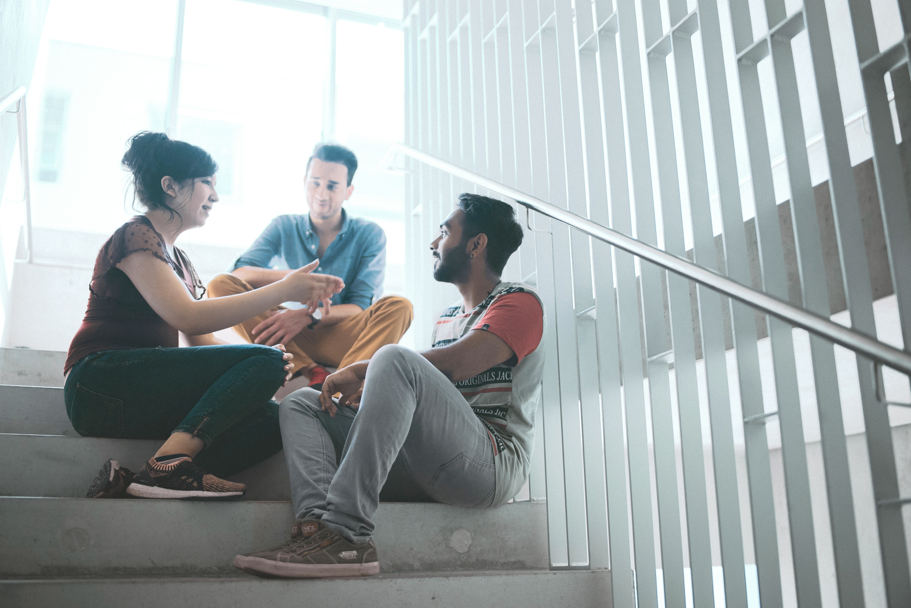 Auf einer Treppe in der Hochschule sitzen drei Studierende und unterhalten sich