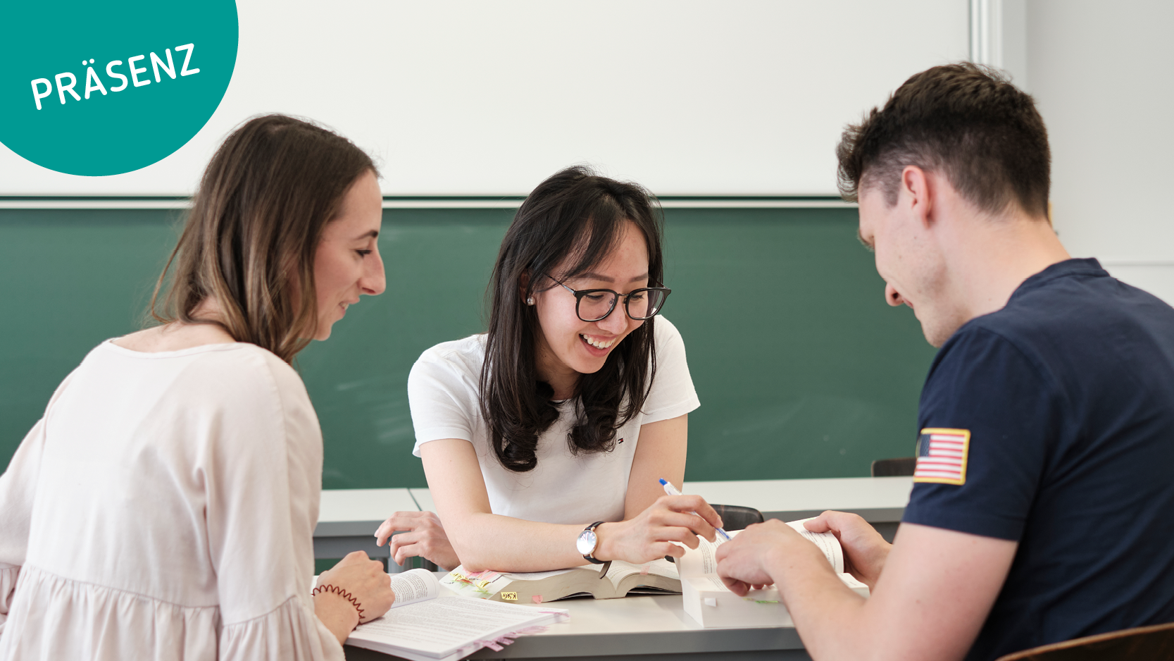 Drei Studierende sitzen im Klassenzimmer und arbeiten gemeinsam