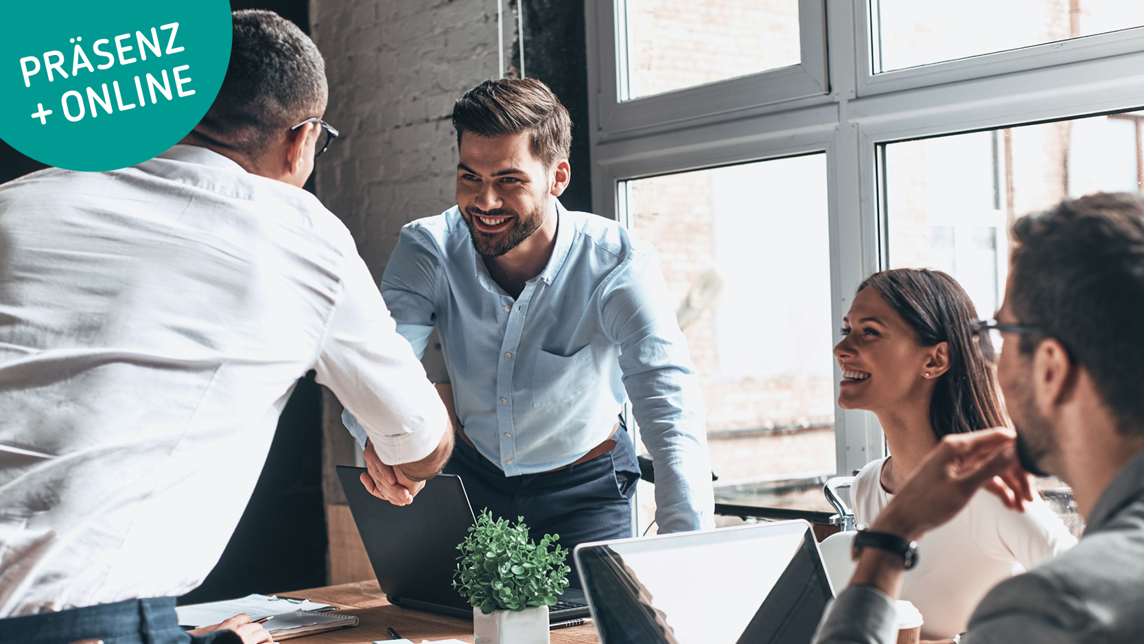 Vier Menschen bei einem Business-Meeting, zwei Männer geben sich die Hand und lächeln