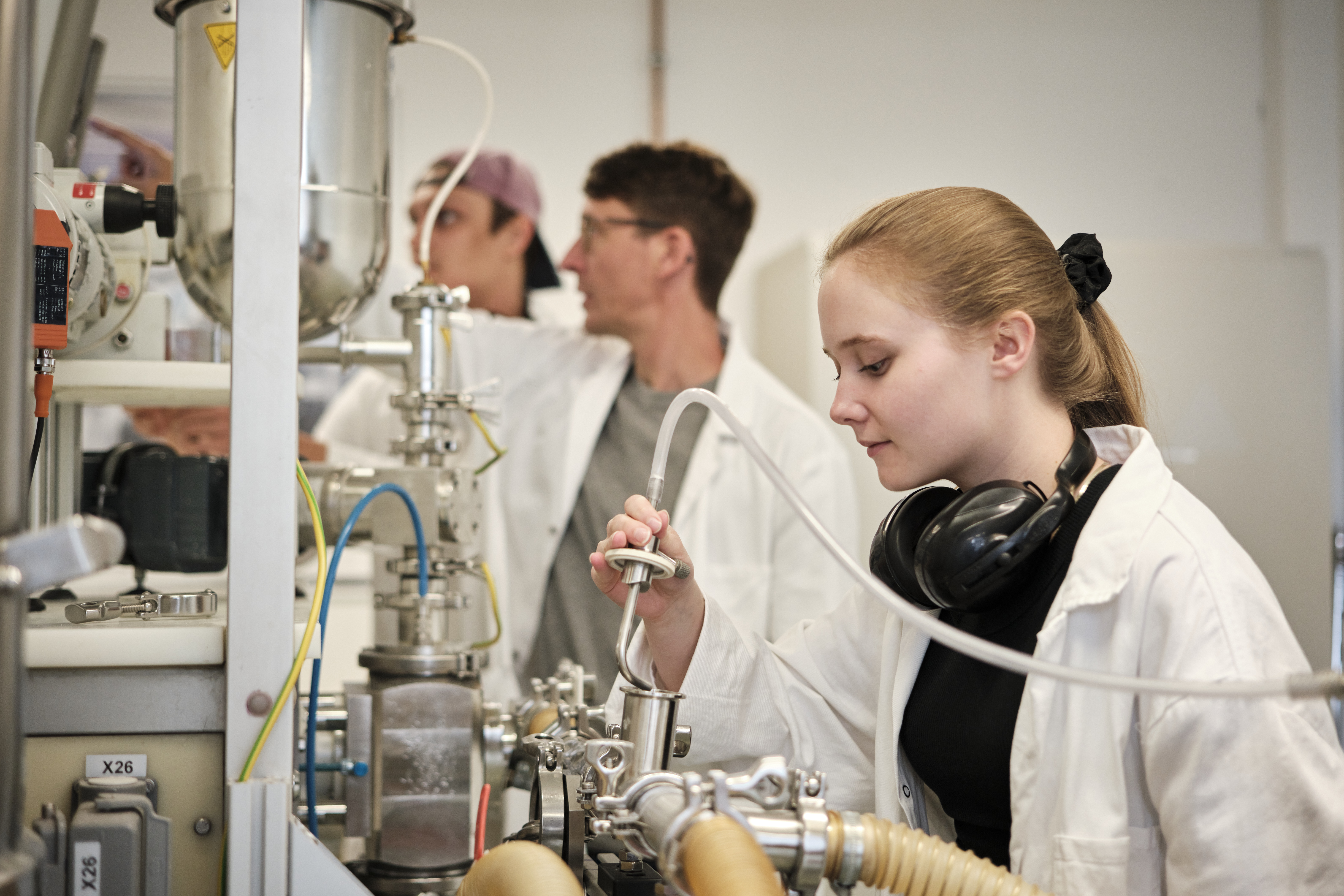 Studierende in weißen Kitteln im Labor. Eine Studentin füllt Flüssigkeit um.