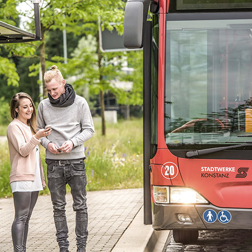 Zwei Studierende unterhalten sich an der Bushaltestelle