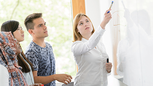 Student explains something to a fellow student on a white board 