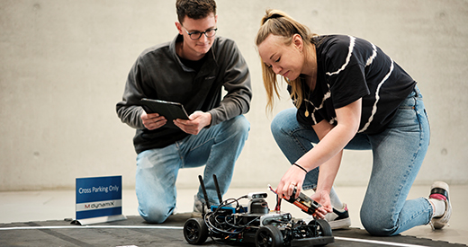 Student und Studentin setzen Modellauto auf Bahn