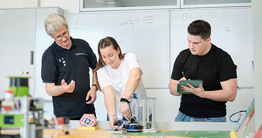 Lehrender und zwei Studierende arbeiten an einem Roboter