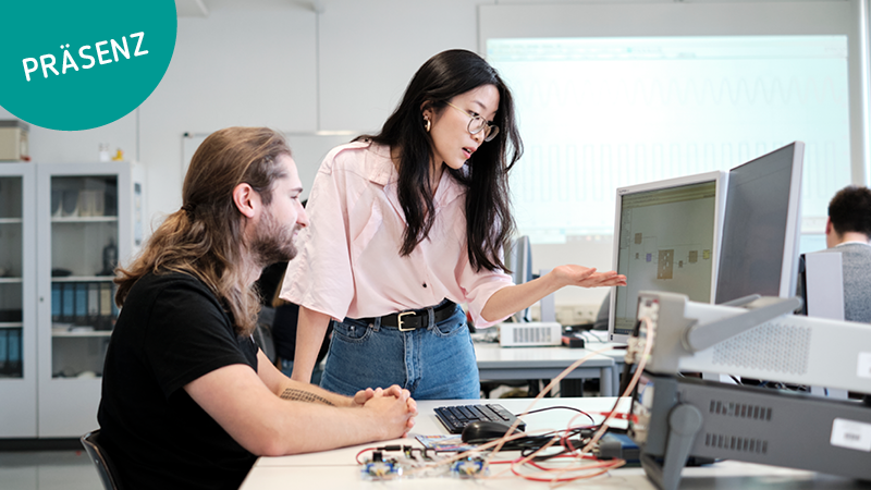 Zwei Studierende besprechen etwas und schauen auf den Bildschirm eines Computers